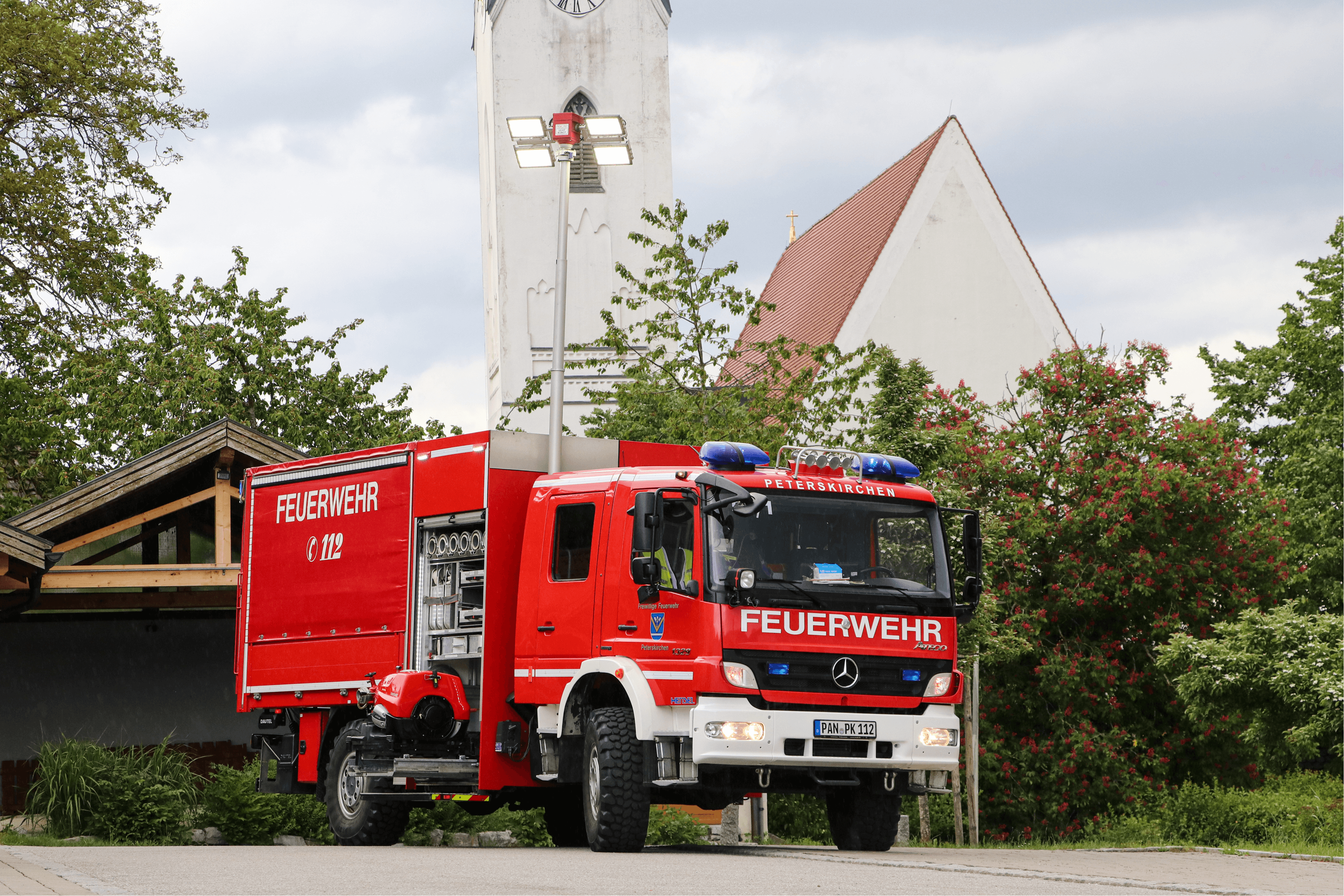 Gerätewagen mit ausgefahrenem Lichtmast vor dem Kirchturm Peterskirchen